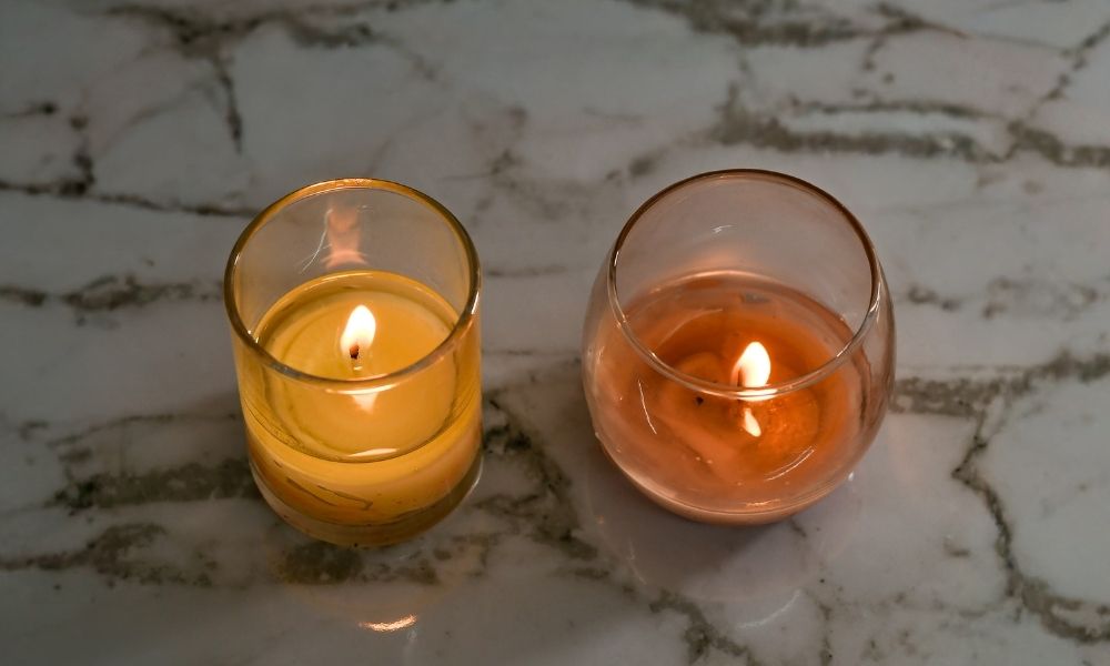 Two lit votive candles, one in a narrow cup and one in a wider cup