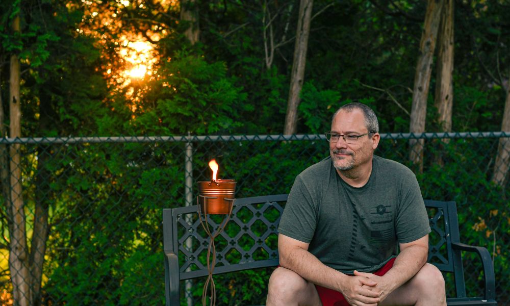 Man sitting outside next to a citronella bucket candle
